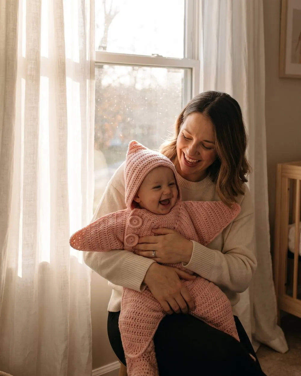 Mother holding her baby in a blush pink star suit by the window