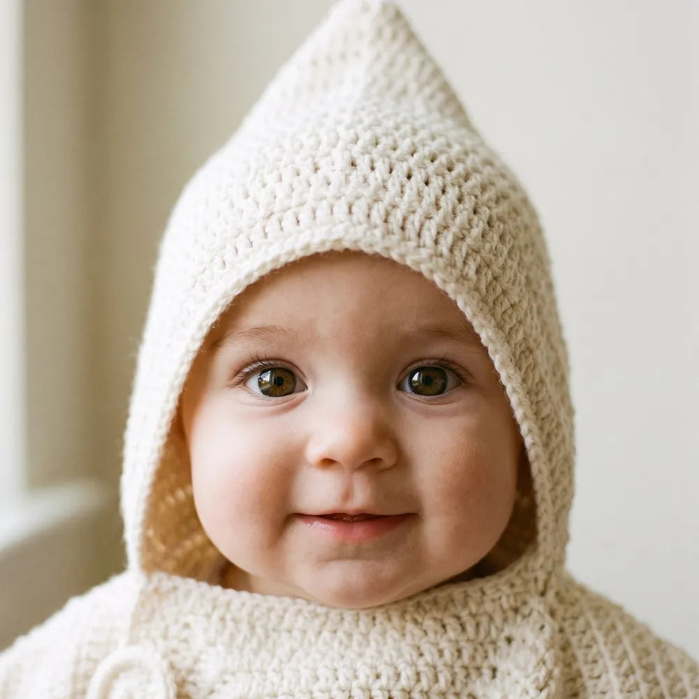 Baby peeking out of a cream crochet hood