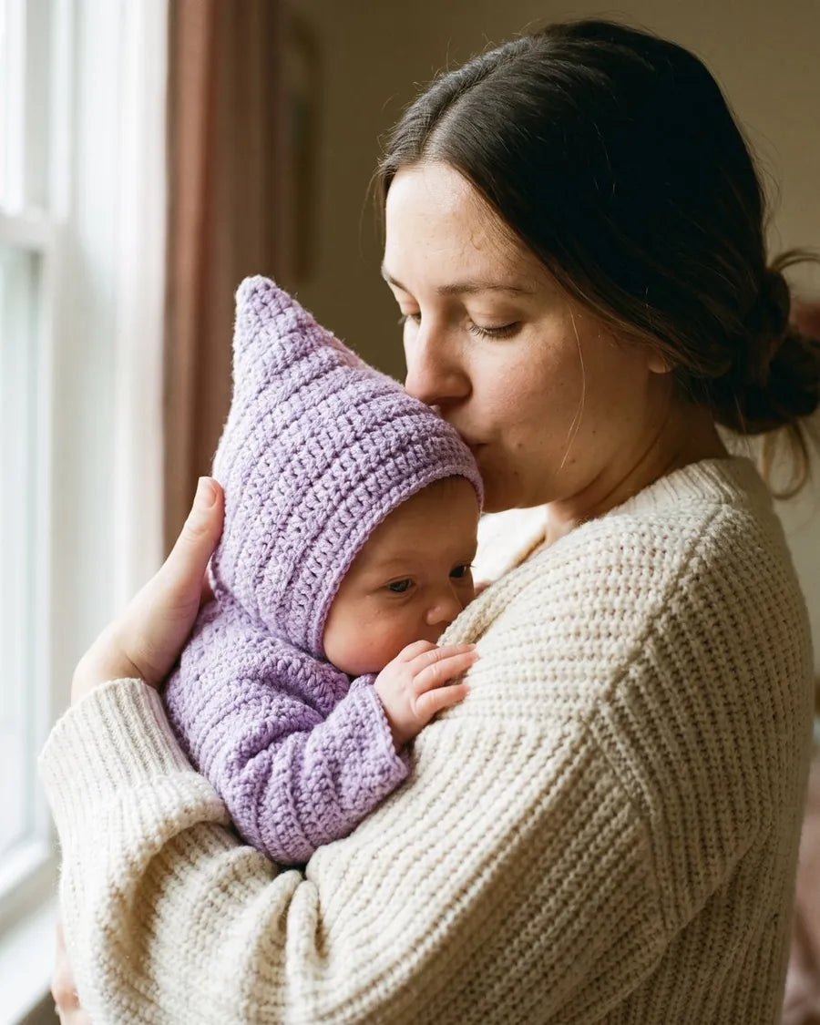 Mother kissing her baby wearing a lavender crochet star suit